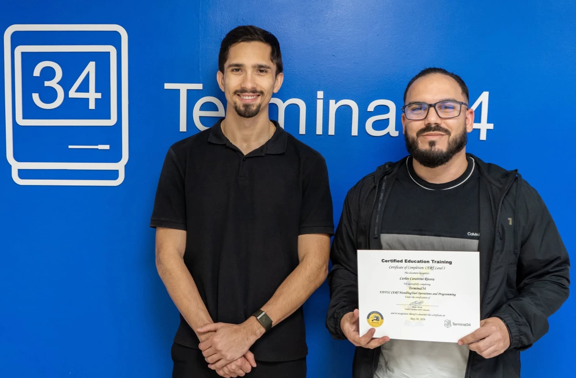 Graduado del curso de Robótica Industrial FANUC con espejuelos y su certificado junto al instructor