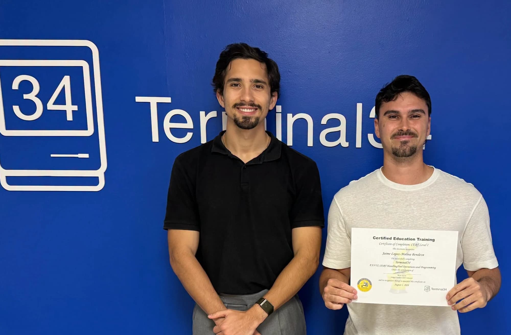 Graduado del curso de Robótica Industrial FANUC con camiseta blanca y su certificado junto al instructor