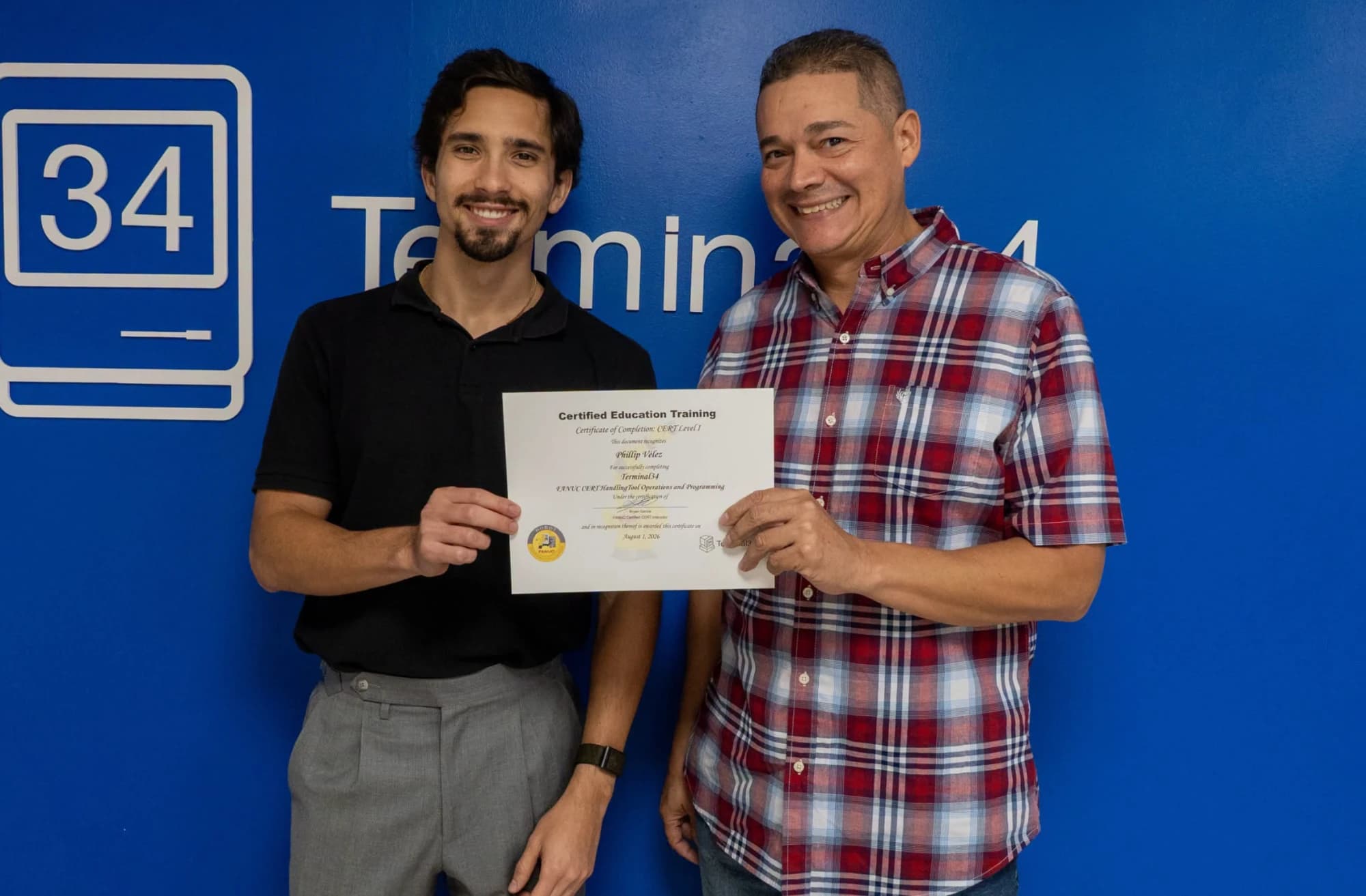 Graduado del curso de Robótica Industrial FANUC con camisa de cuadros recibiendo su certificado