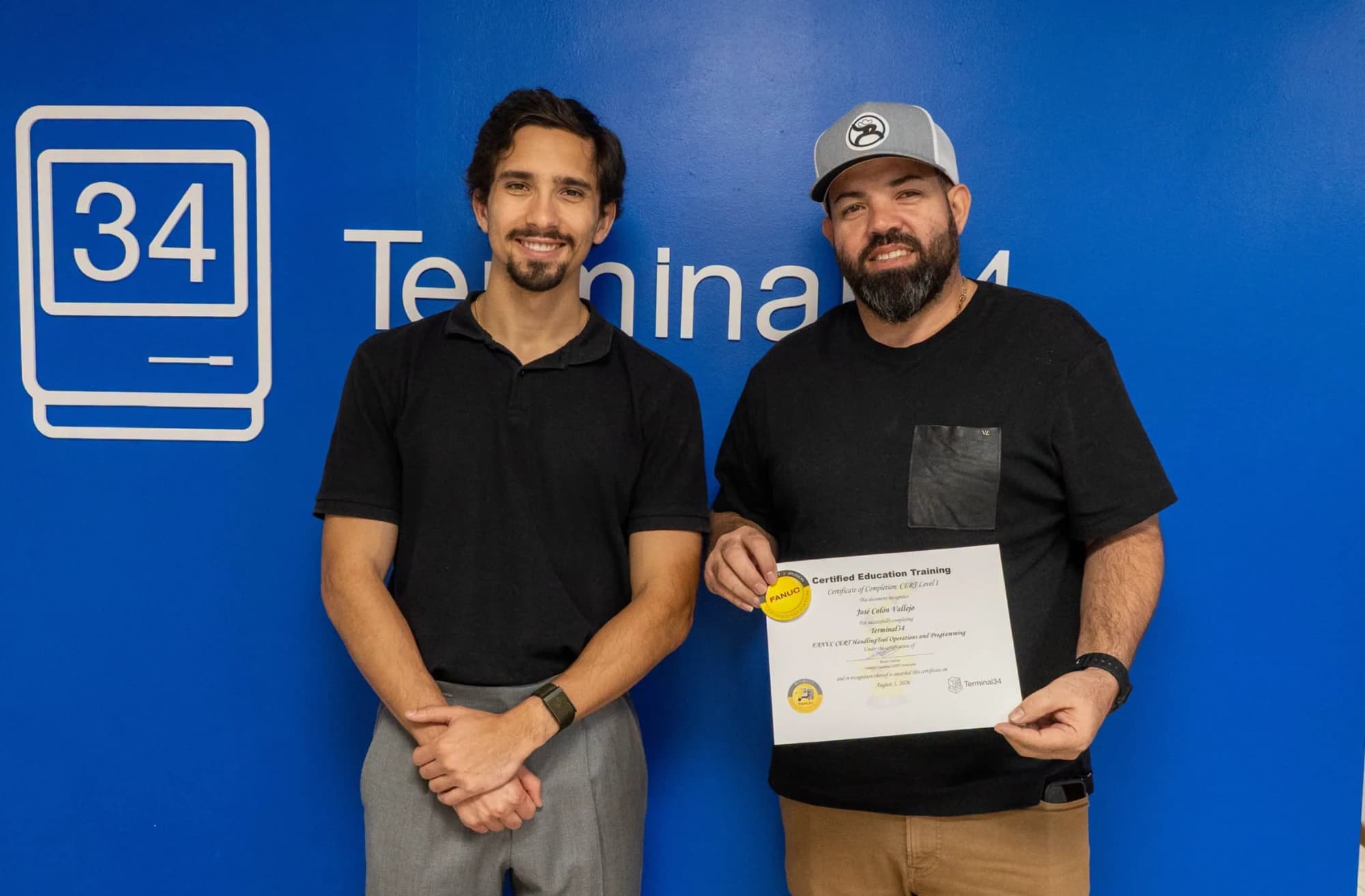 Graduado del curso de Robótica Industrial FANUC con gorra y su certificado junto al instructor